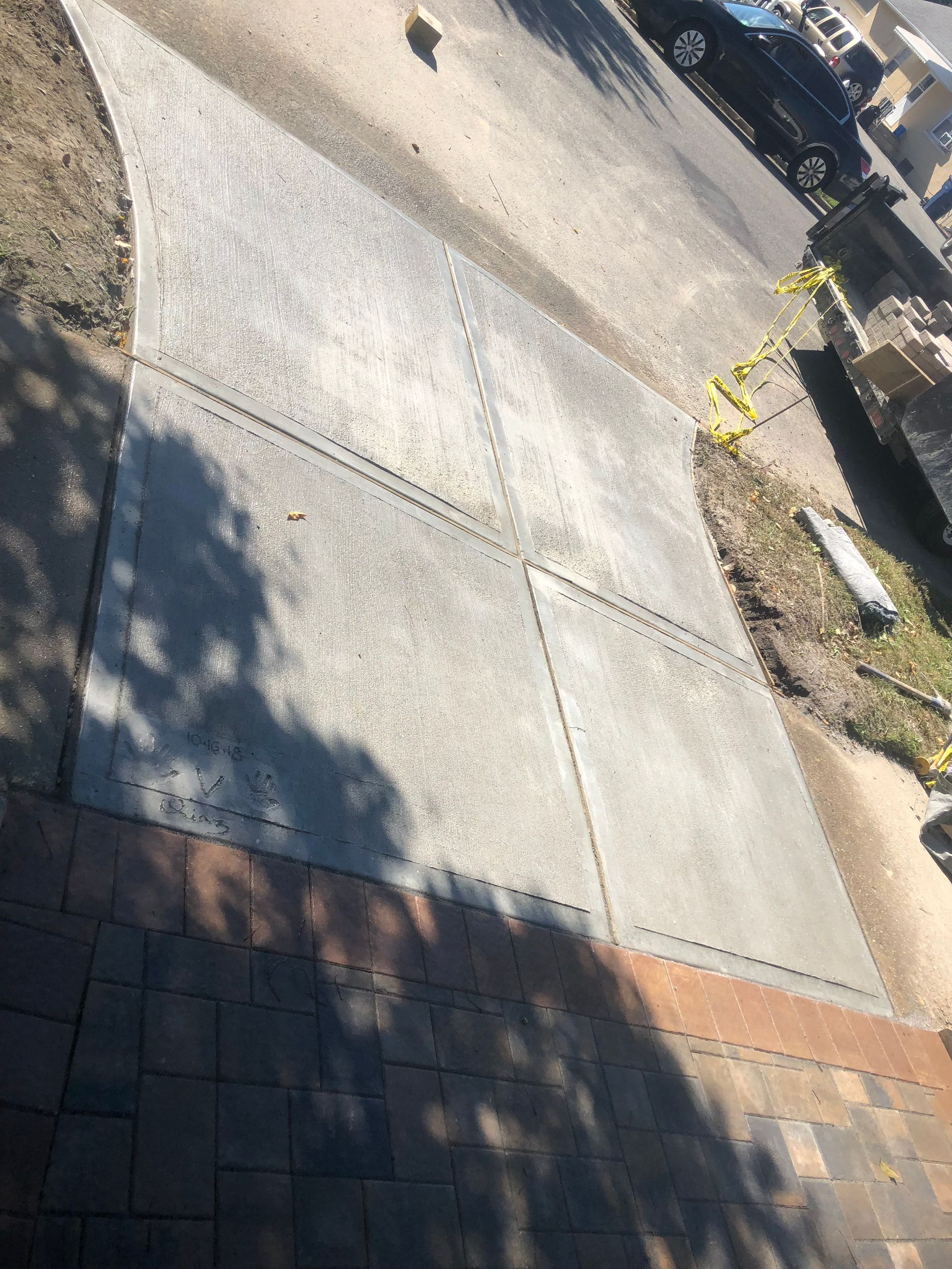 Concrete driveway with visible expansion joints, partially shadowed by a building and trees.