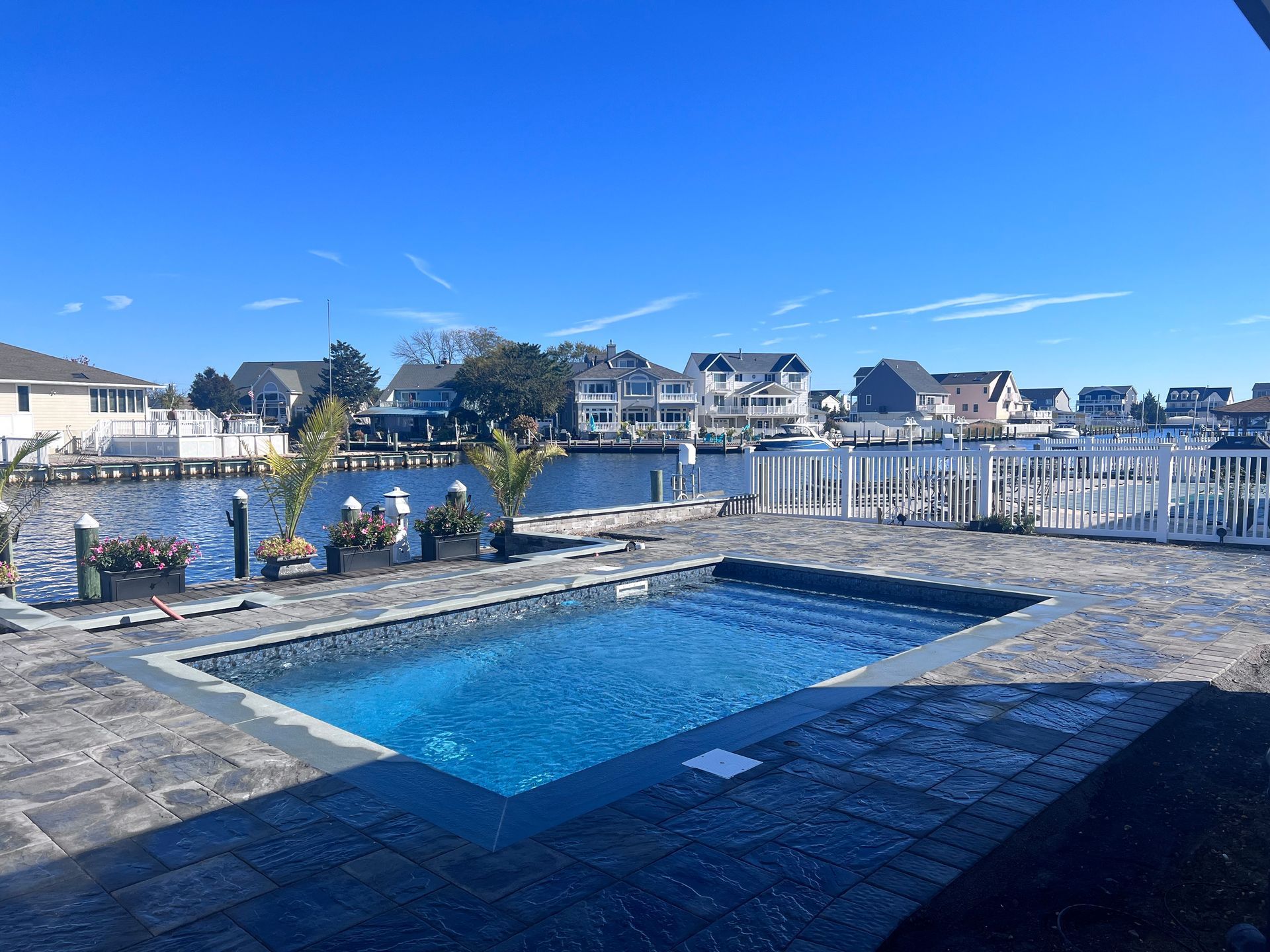 Pool overlooking a waterway with docks and homes under a blue sky.