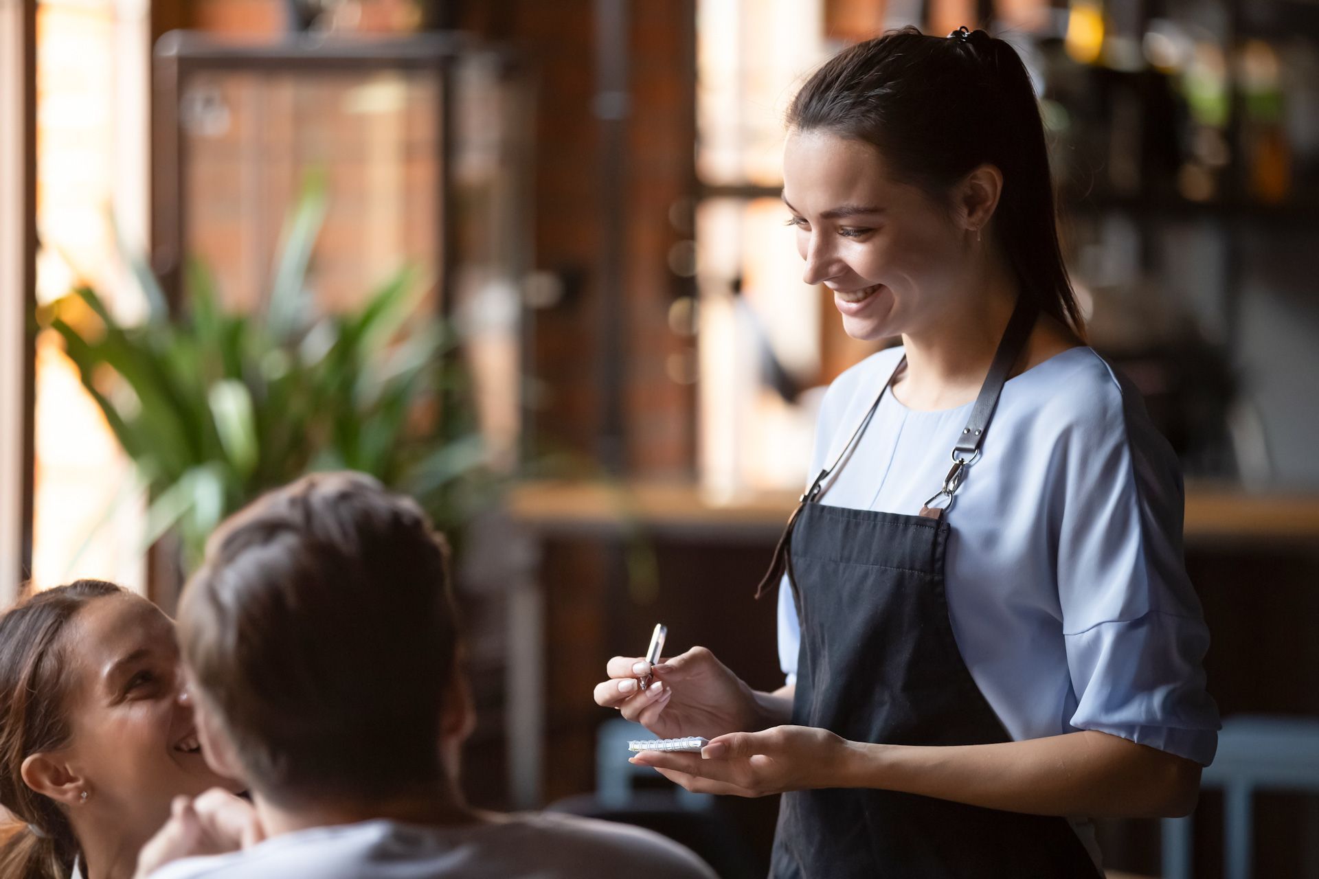 A waitress is taking a order from a man and a woman in a restaurant.