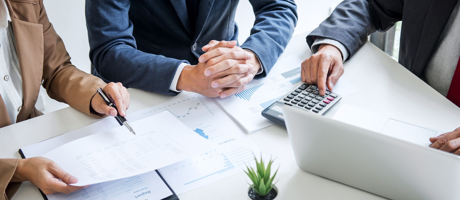 A group of business people are sitting at a table with a laptop and a calculator.