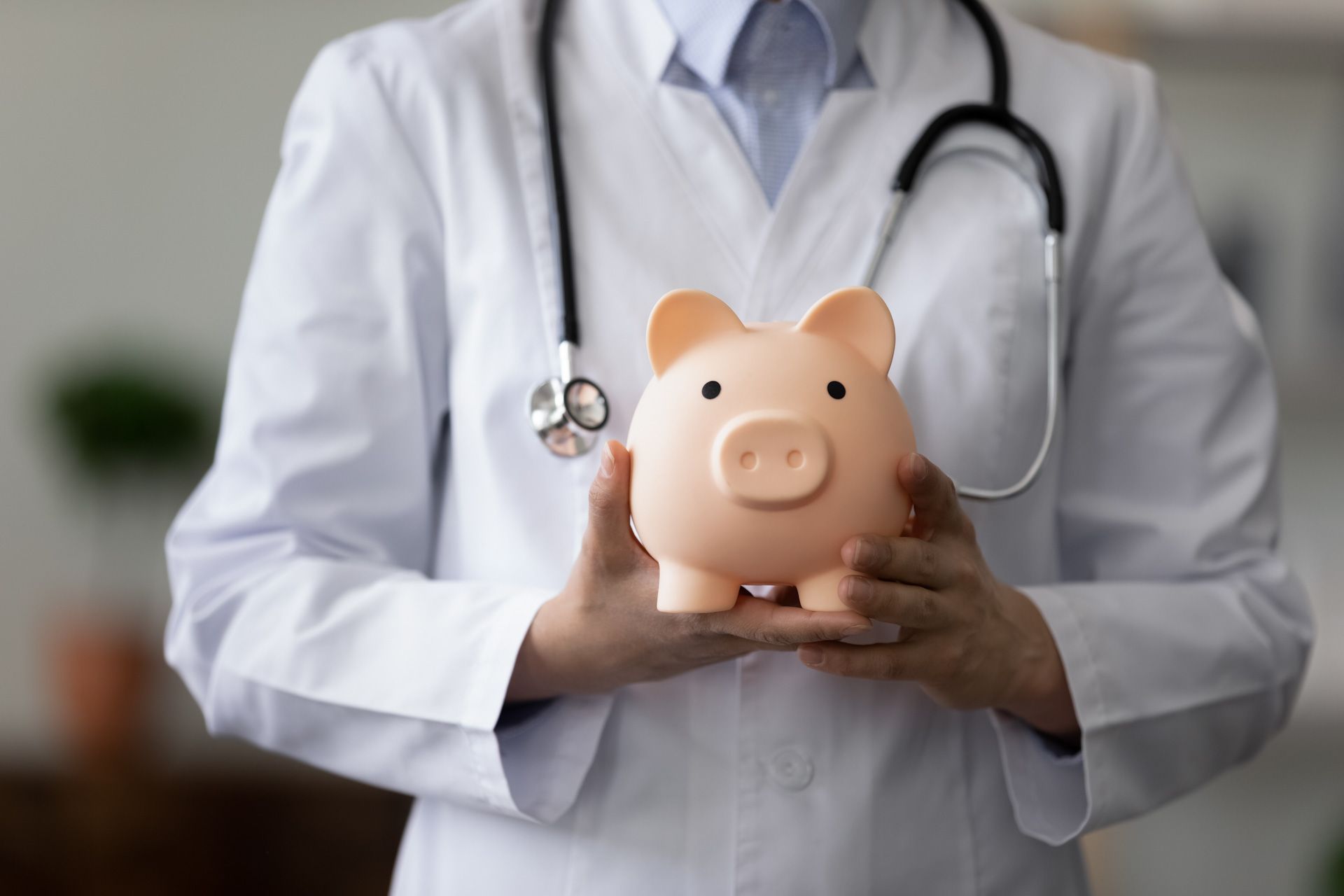 A doctor is holding a piggy bank with a stethoscope around his neck.