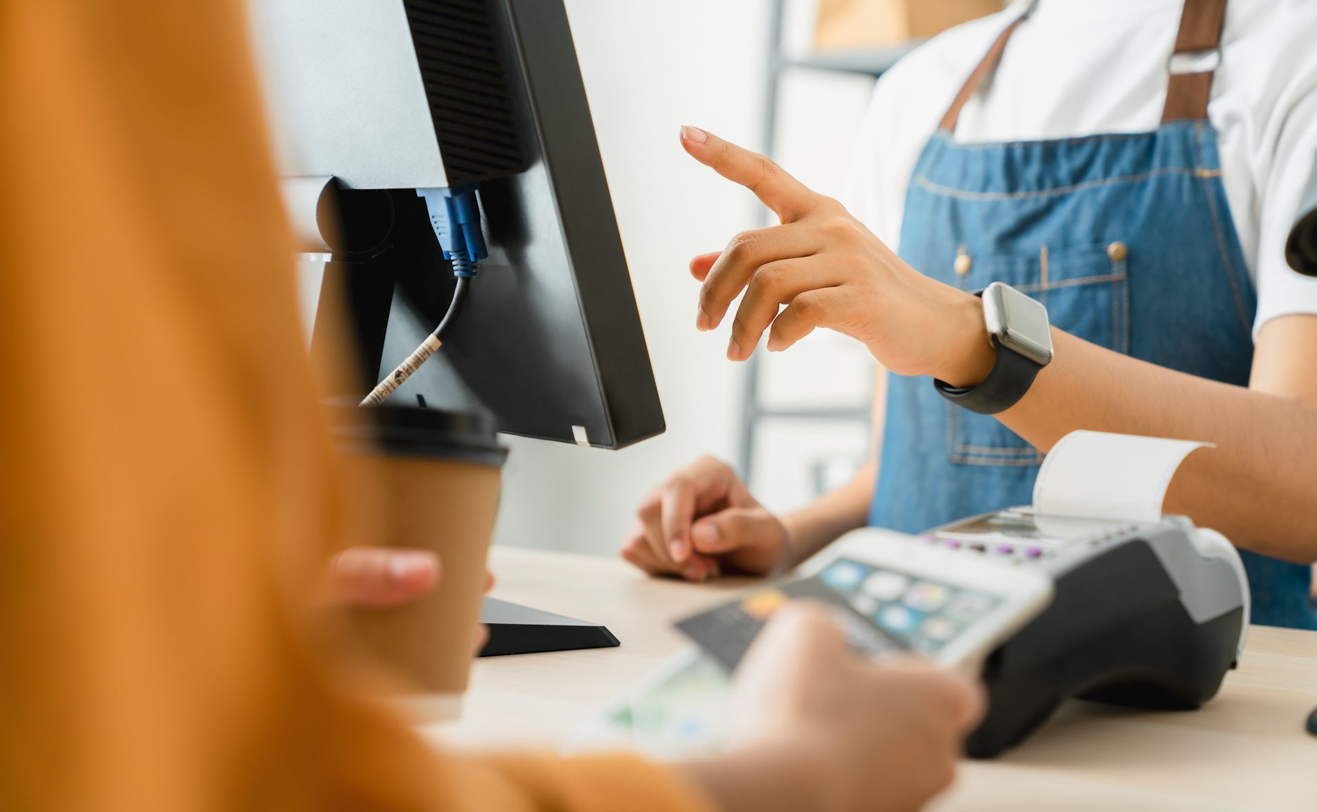 A woman is pointing at a computer screen while another woman is using a credit card machine.