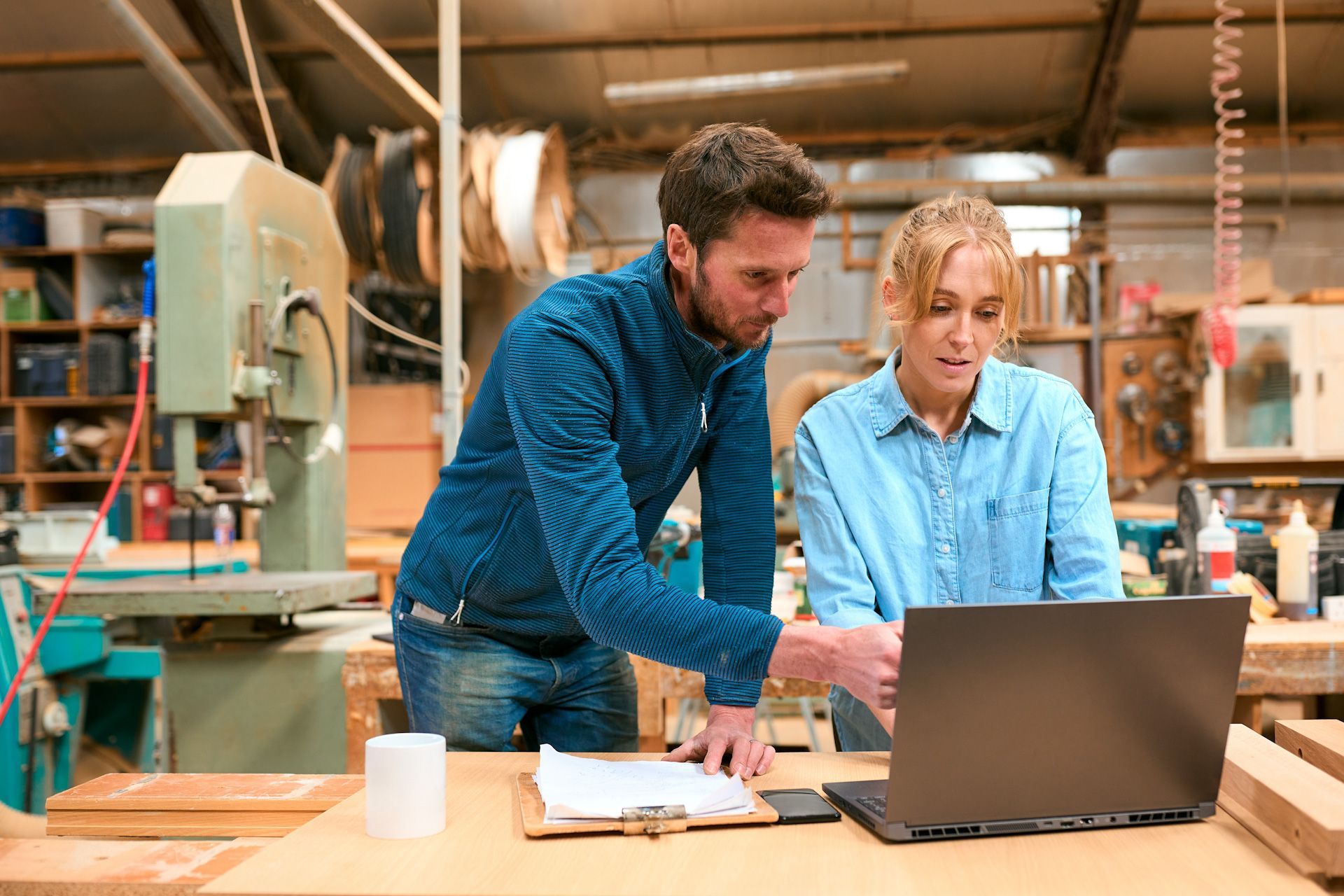 A man and a woman are looking at a laptop computer in a workshop.