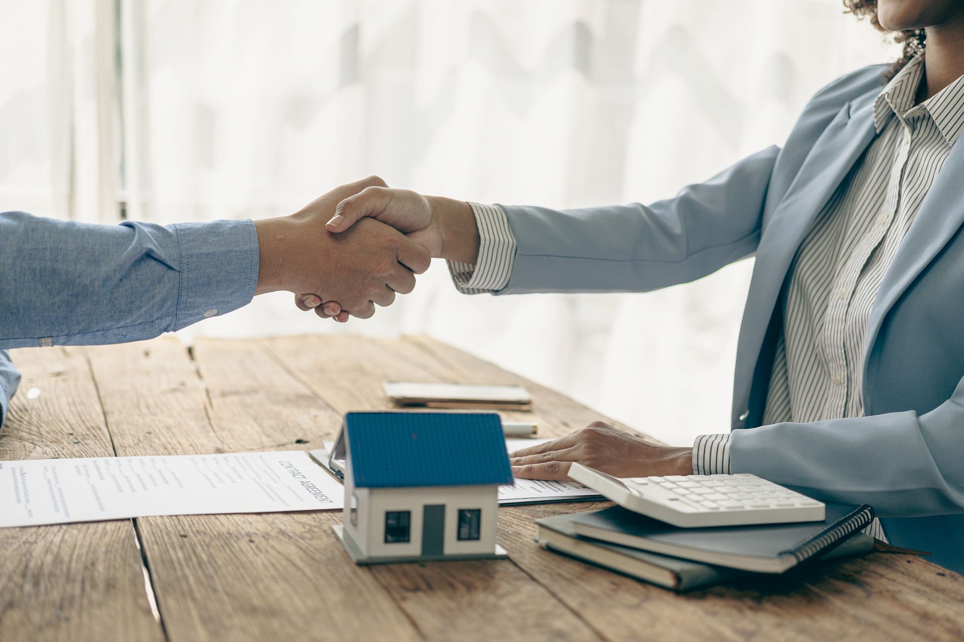 A woman is shaking hands with a man in front of a model house.