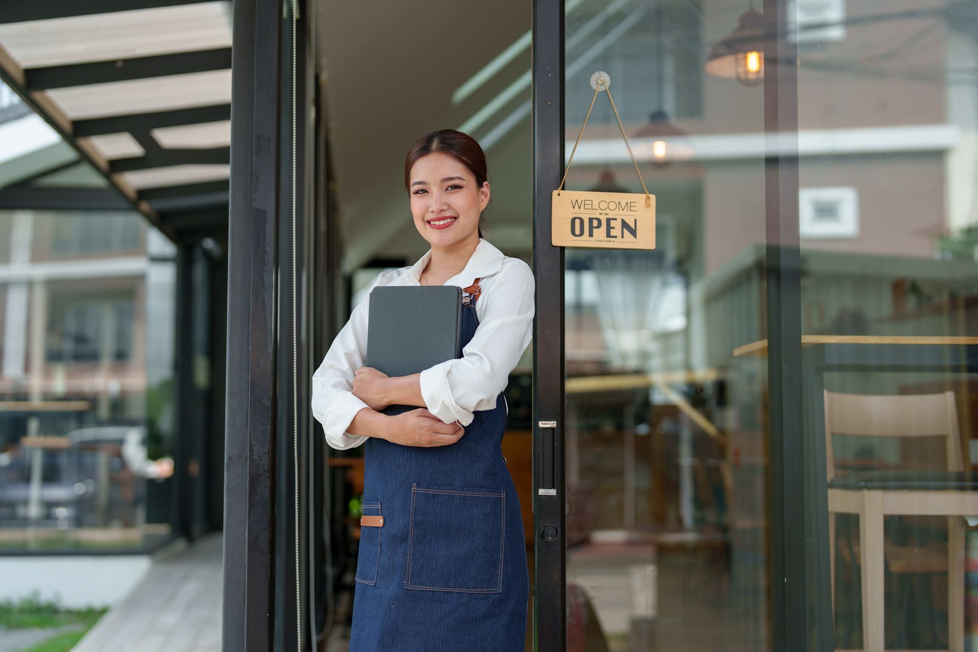 A woman is standing in front of a restaurant holding a tablet.