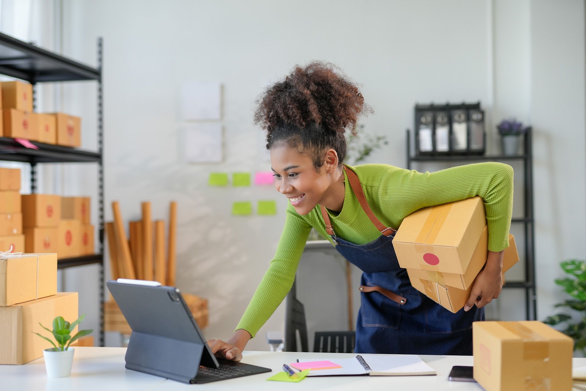 A woman is holding a box and using a tablet computer.