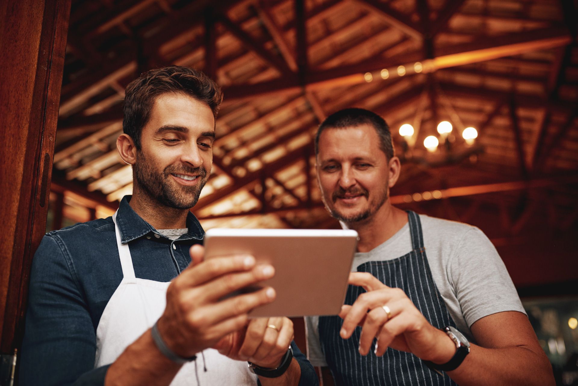 Two men are looking at a tablet in a restaurant.