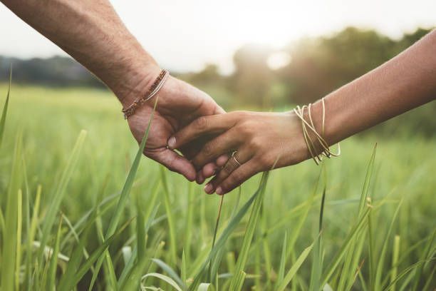 A man and a woman are holding hands in a field of tall grass.
