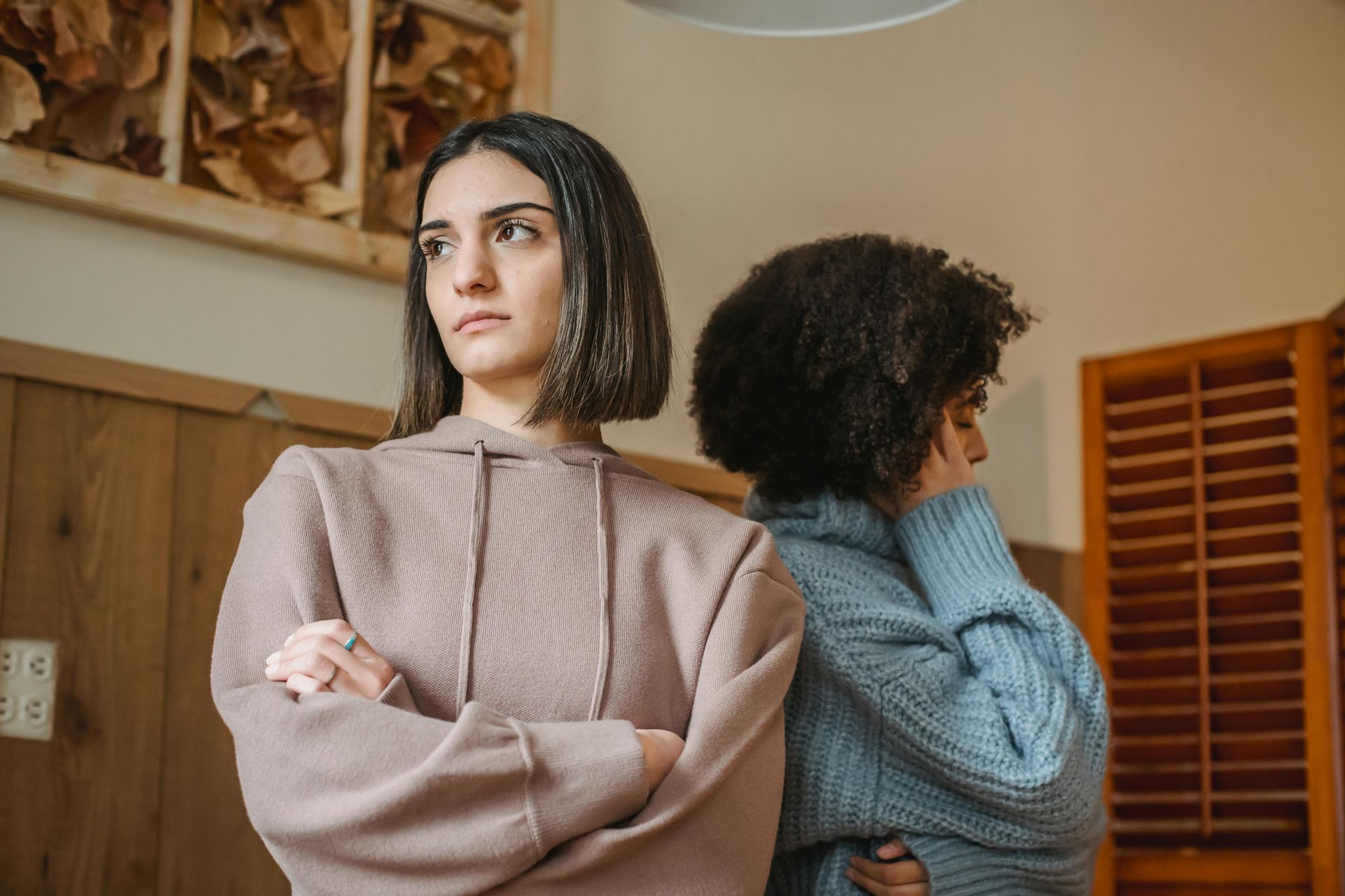 Two women are standing back to back with their arms crossed.