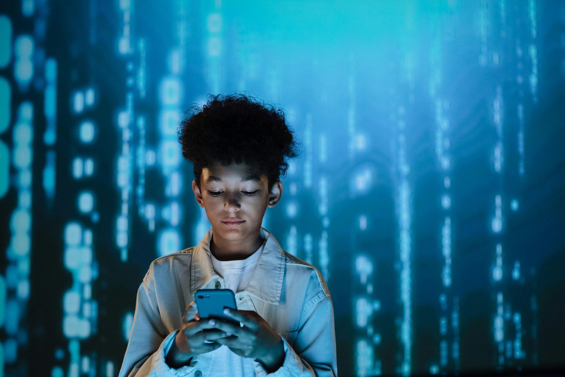 A young boy is using a cell phone in front of a blue background.