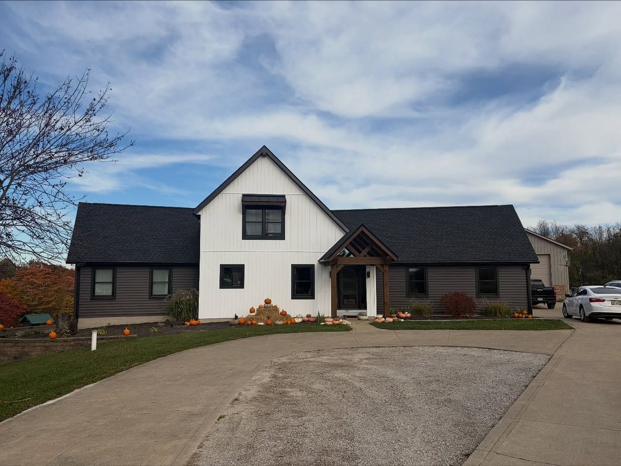 White house with dark roof and gravel driveway under a cloudy blue sky