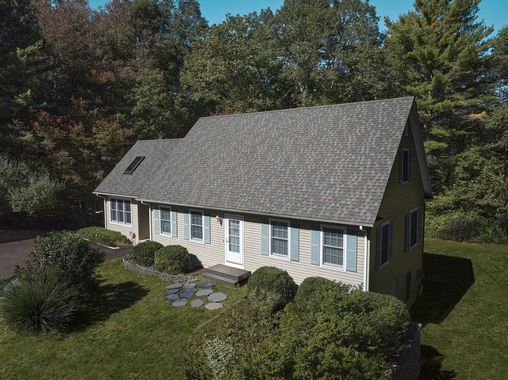 Suburban house with gray roof and white siding, surrounded by trees and shrubs.