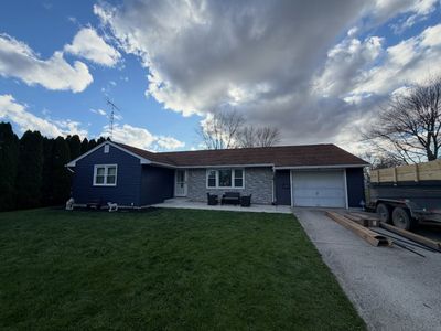 Single-story blue house with garage, gravel driveway, and cloudy sky at dusk