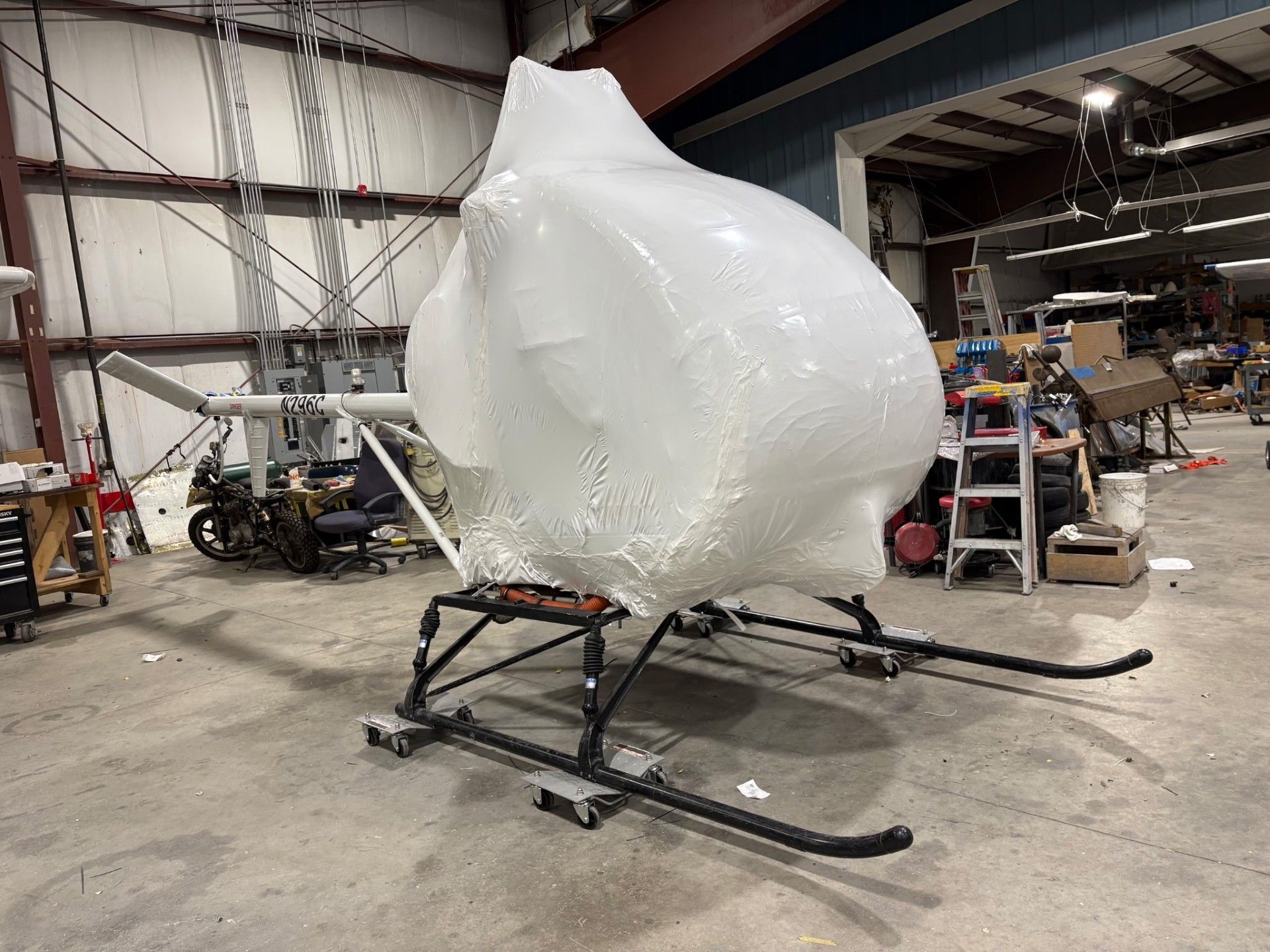 Small helicopter wrapped in white plastic inside a workshop, ready for transport.