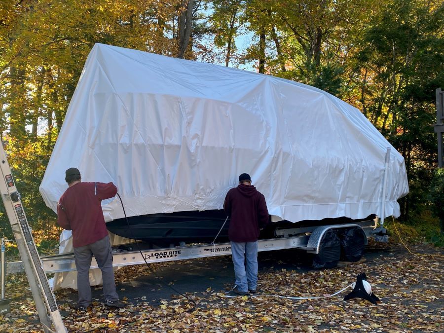 Two men are covering a boat on a trailer with a white tarp.