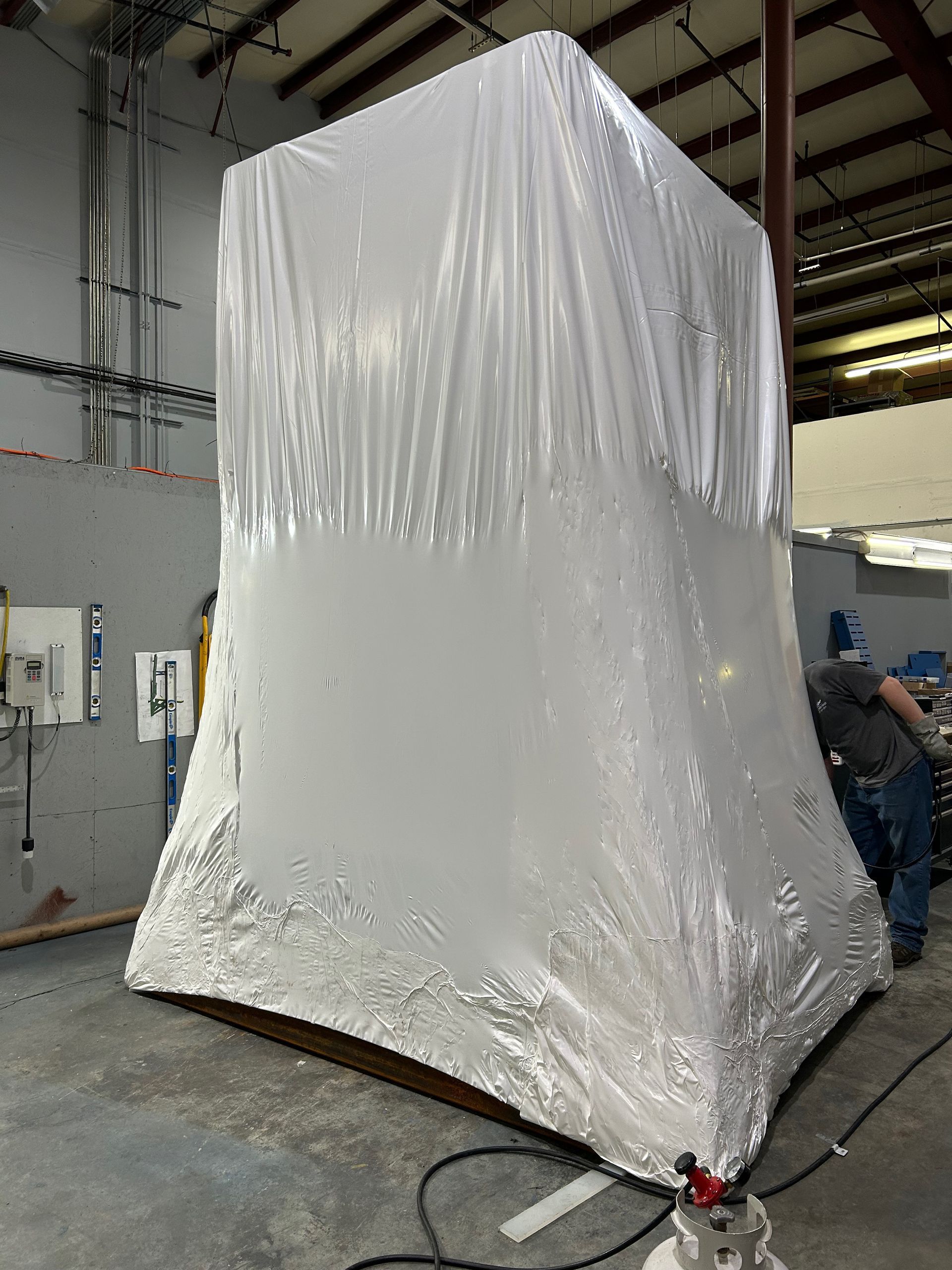 A large object is wrapped in plastic wrap in a warehouse.