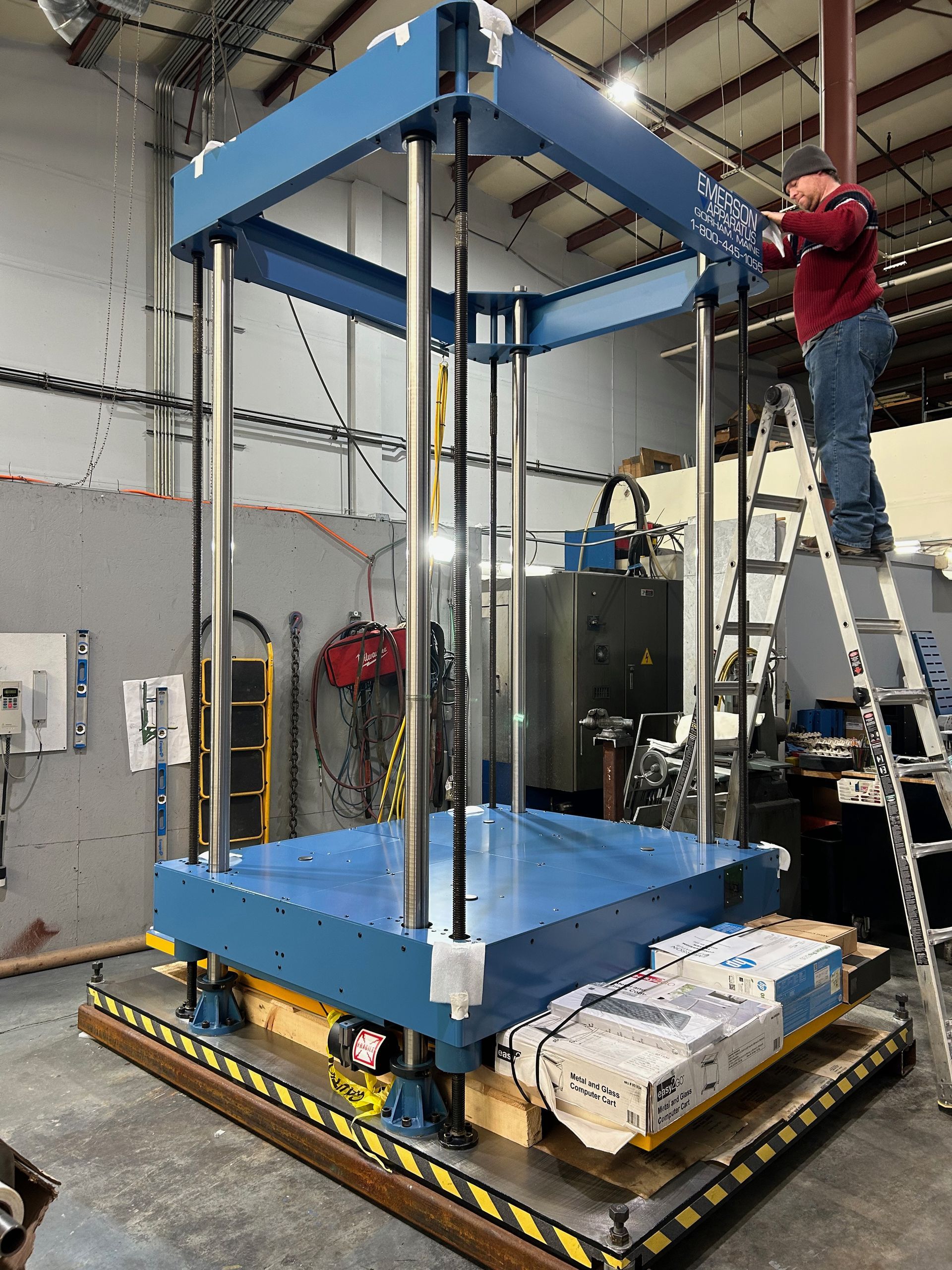 A man on a ladder is working on a machine in a factory