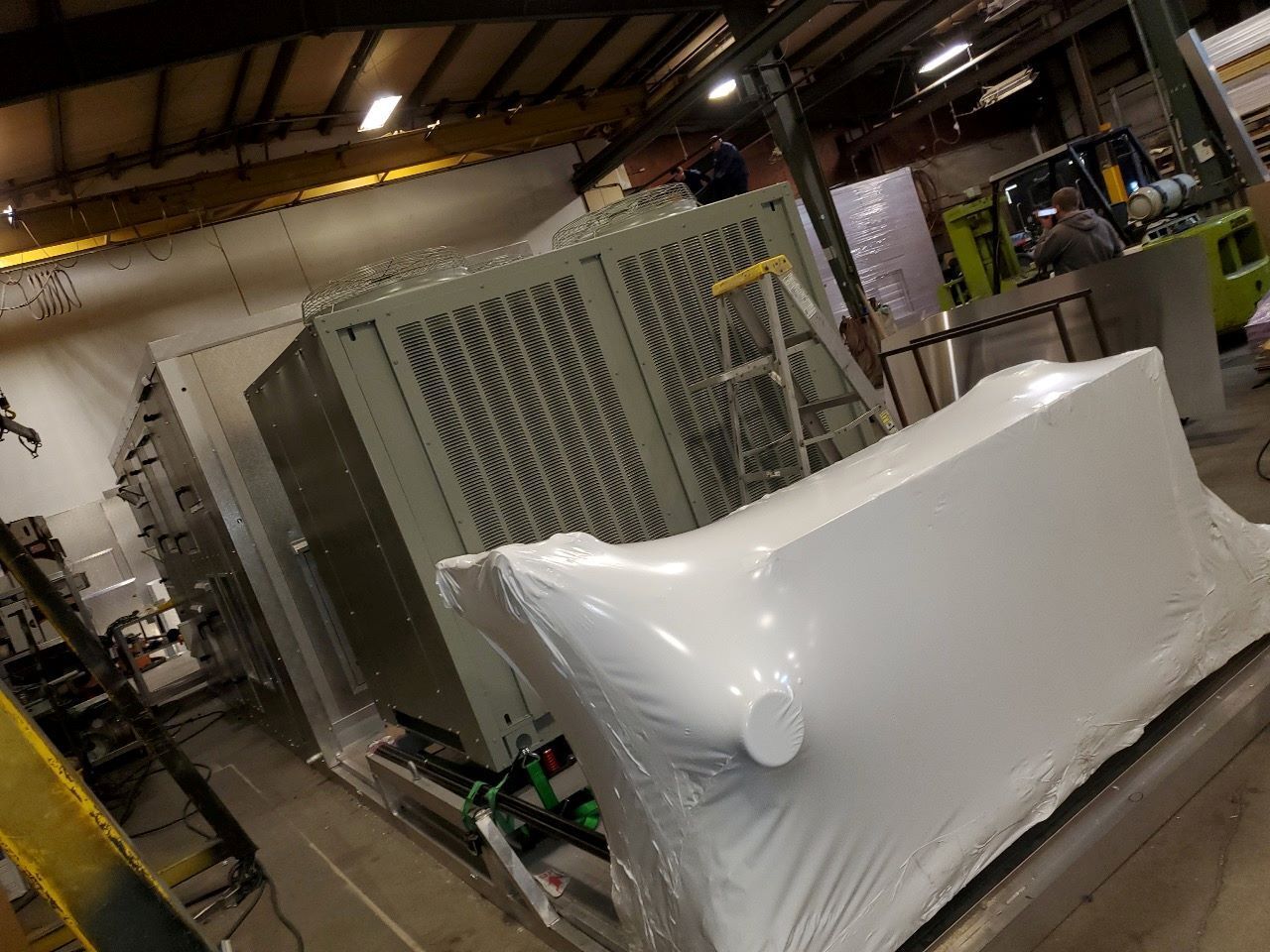 A large piece of equipment is wrapped in plastic in a warehouse.