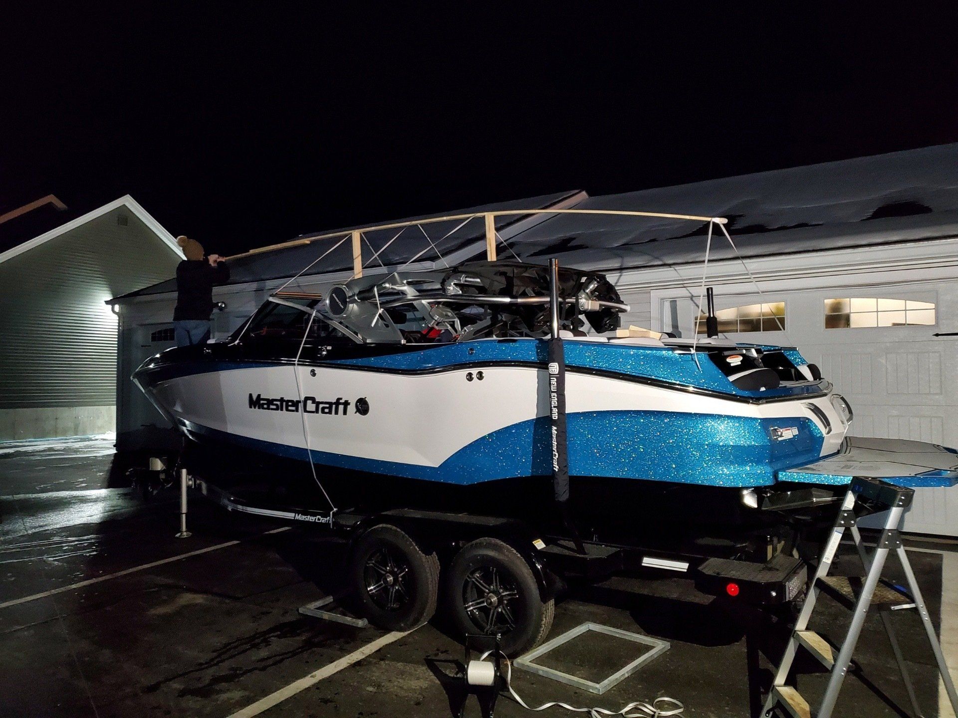 A blue and white boat is on a trailer in a parking lot.