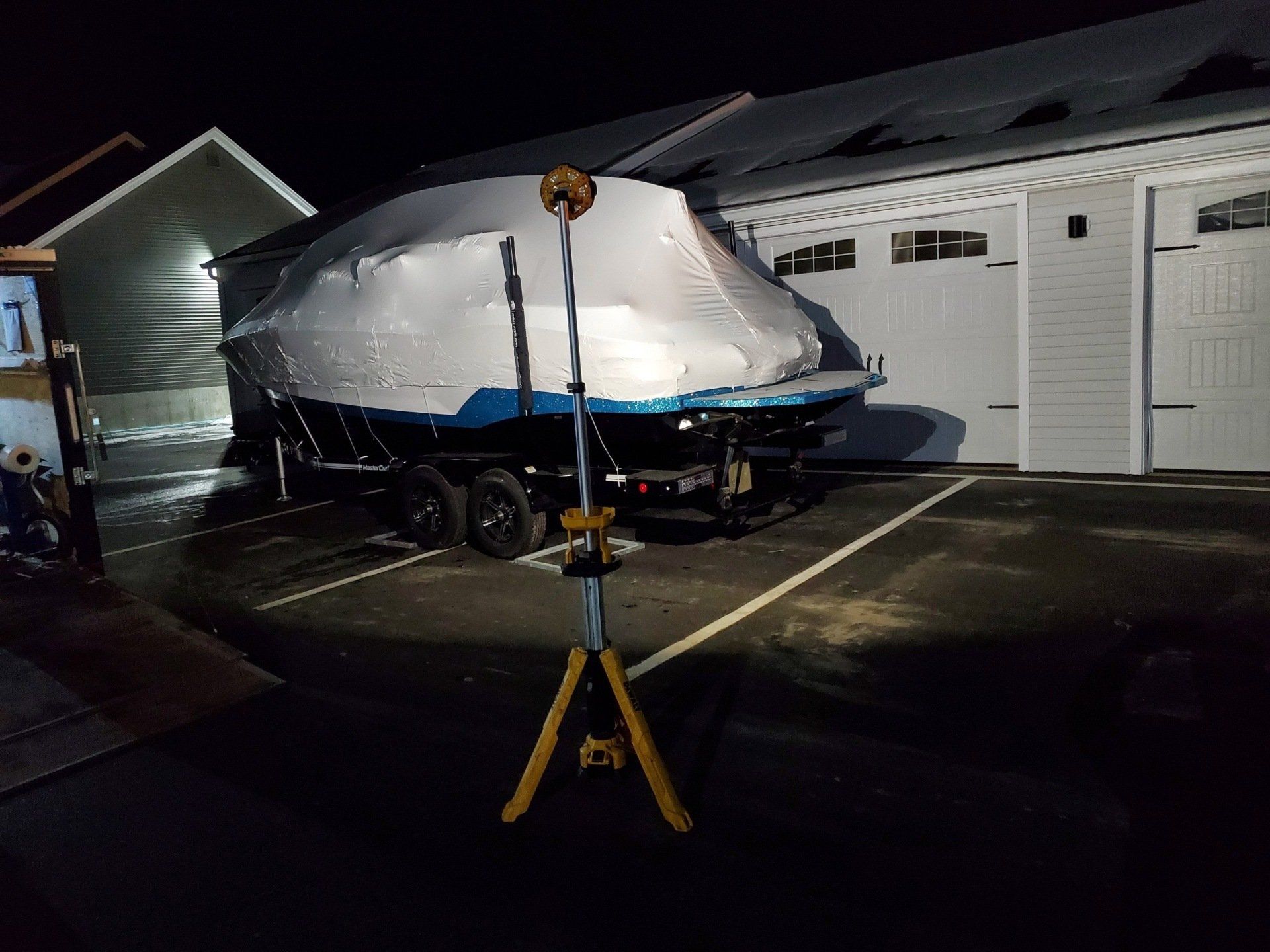 A boat is wrapped in plastic and is parked in front of a garage.