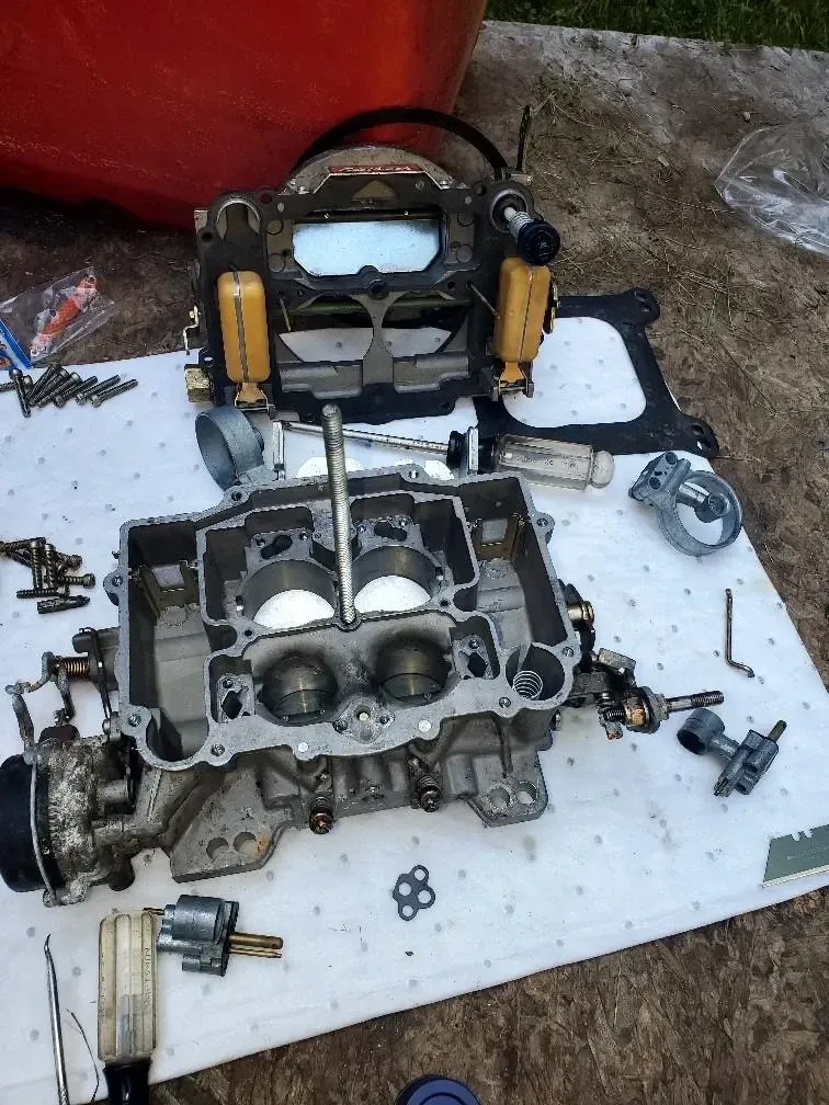 A carburetor is being disassembled on a white mat