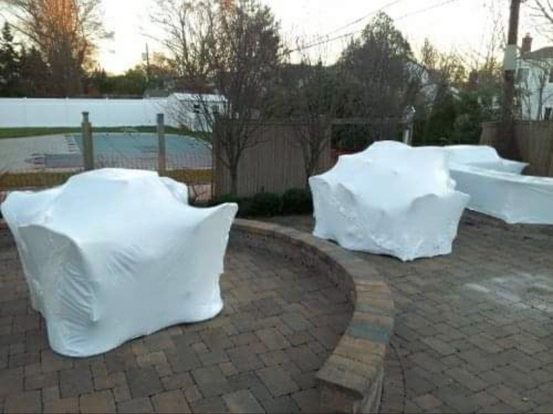 Three chairs are wrapped in plastic wrap on a patio.