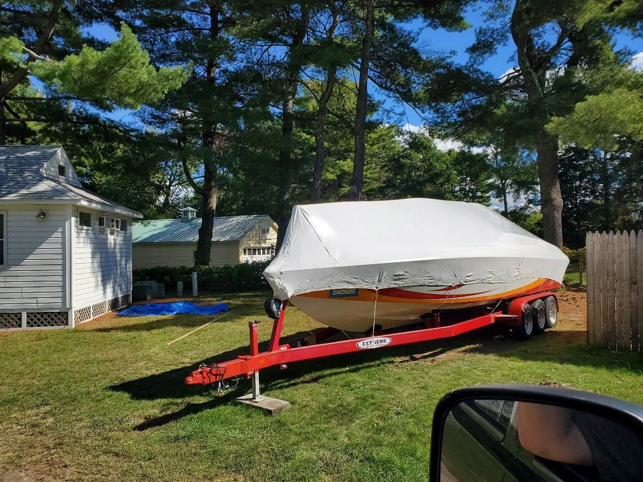 A boat is sitting on a trailer in the grass in front of a house.