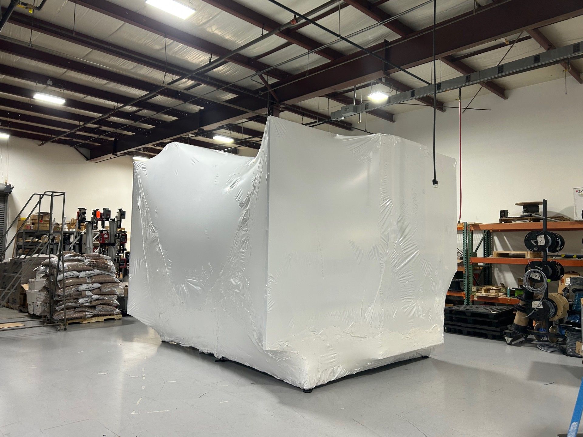 A large white object is wrapped in plastic in a warehouse.