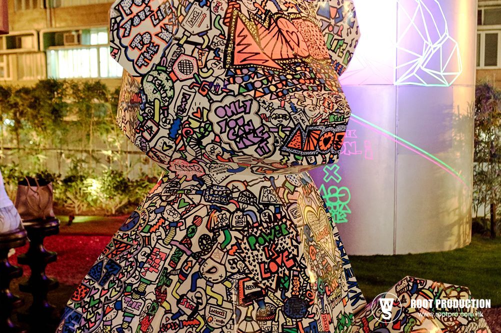 Large, colorful graffiti-covered teddy bear statue in an outdoor setting at night.
