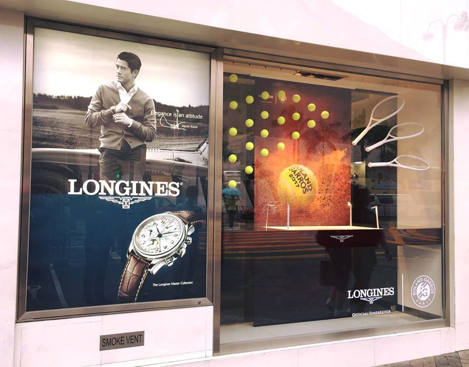 Longines store window display with tennis theme and watch ad, featuring a man, tennis balls, and racquets.