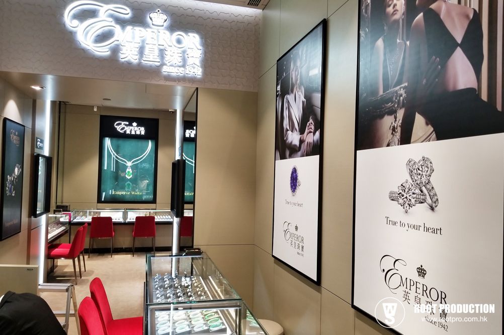Interior view of Emperor jewelry store with displays and posters. Red chairs, beige walls, and jewelry cases.