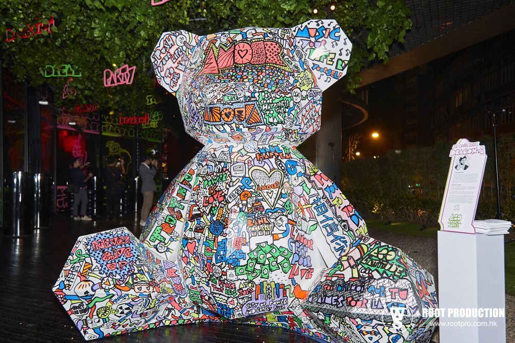 Giant colorful teddy bear sculpture in front of a building with illuminated neon signs.