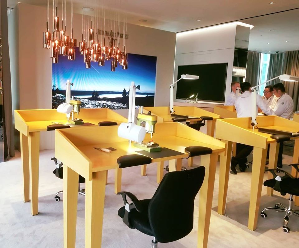 Watchmaking workshop with wooden workstations, focused lighting, and technicians at work.