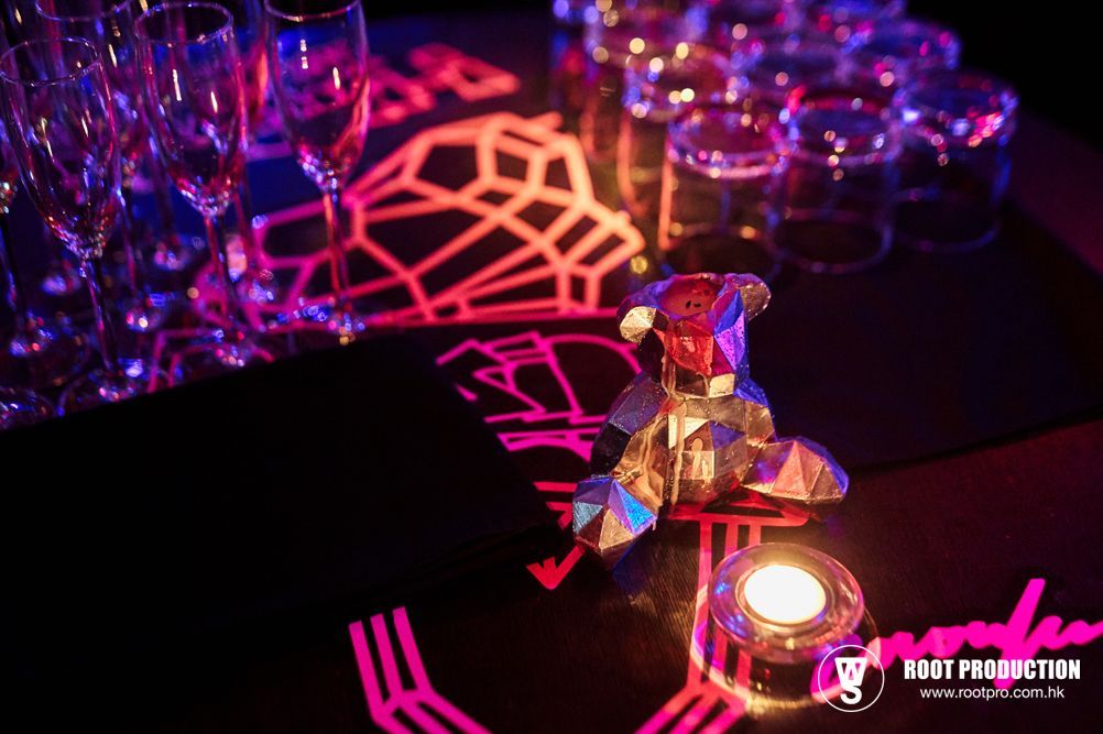 Lit event table with glassware, faceted metal sculpture, candle, and geometric neon lights.