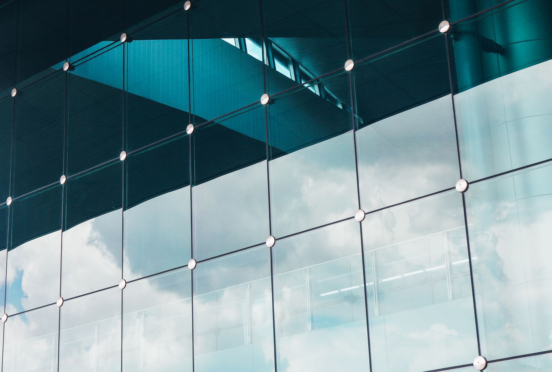 Reflective glass building facade with a metallic grid frame, showing a view of the sky and clouds.
