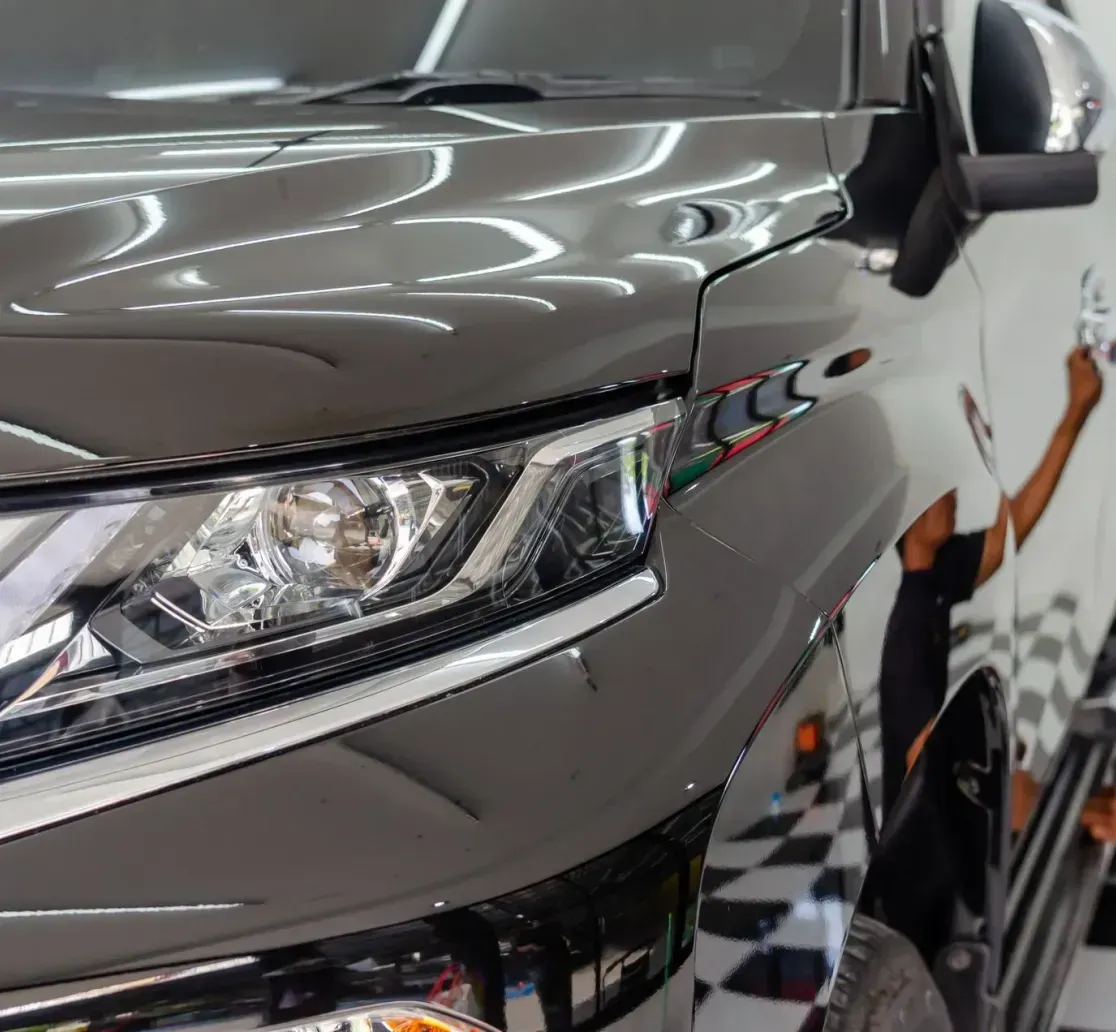 A professional applying a protective film to the side panel of a dark gray pickup truck in a well-lit workshop.