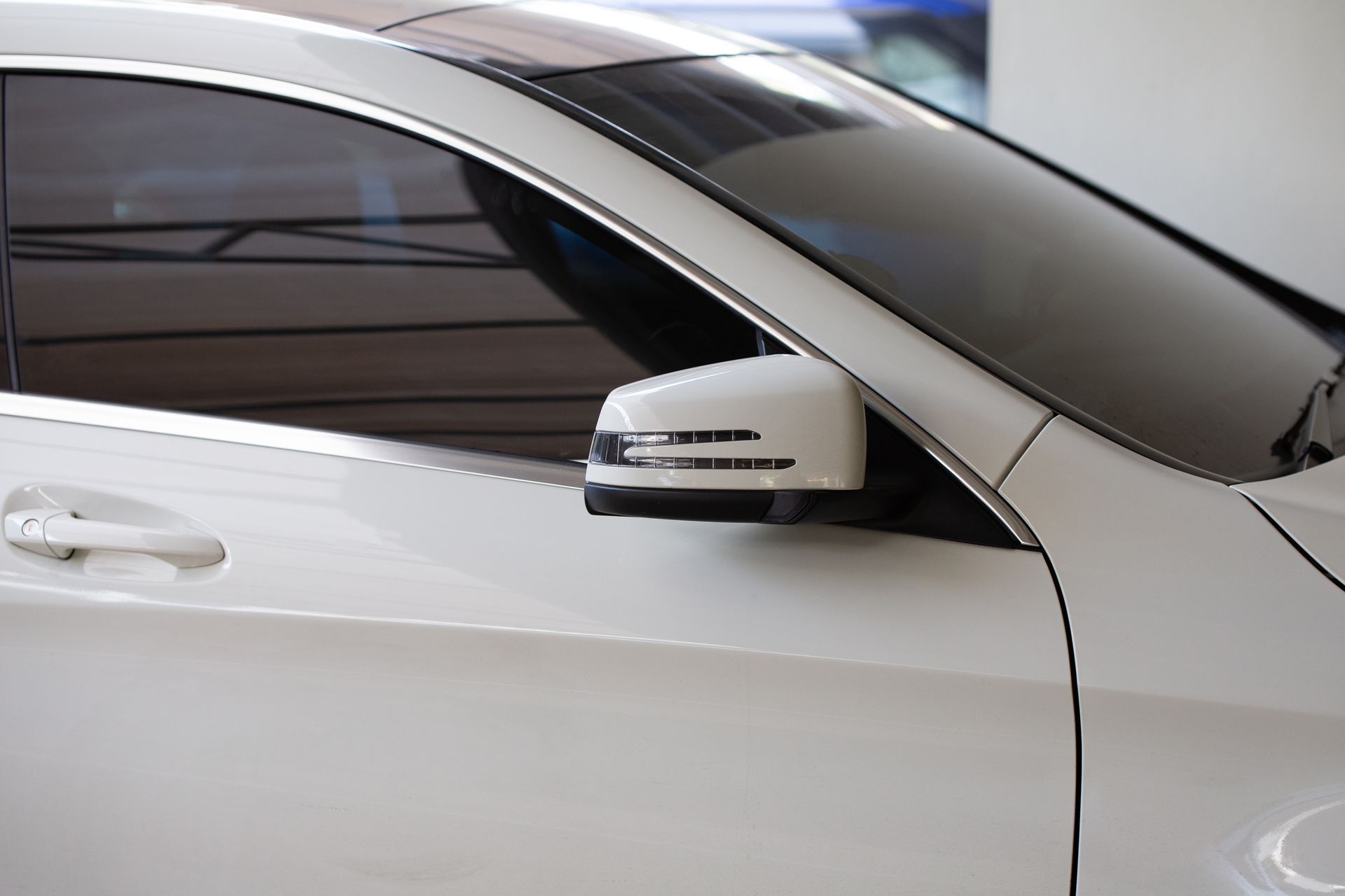 Side view of a white car, focusing on the driver-side door, tinted window, and side mirror with an integrated signal light.
