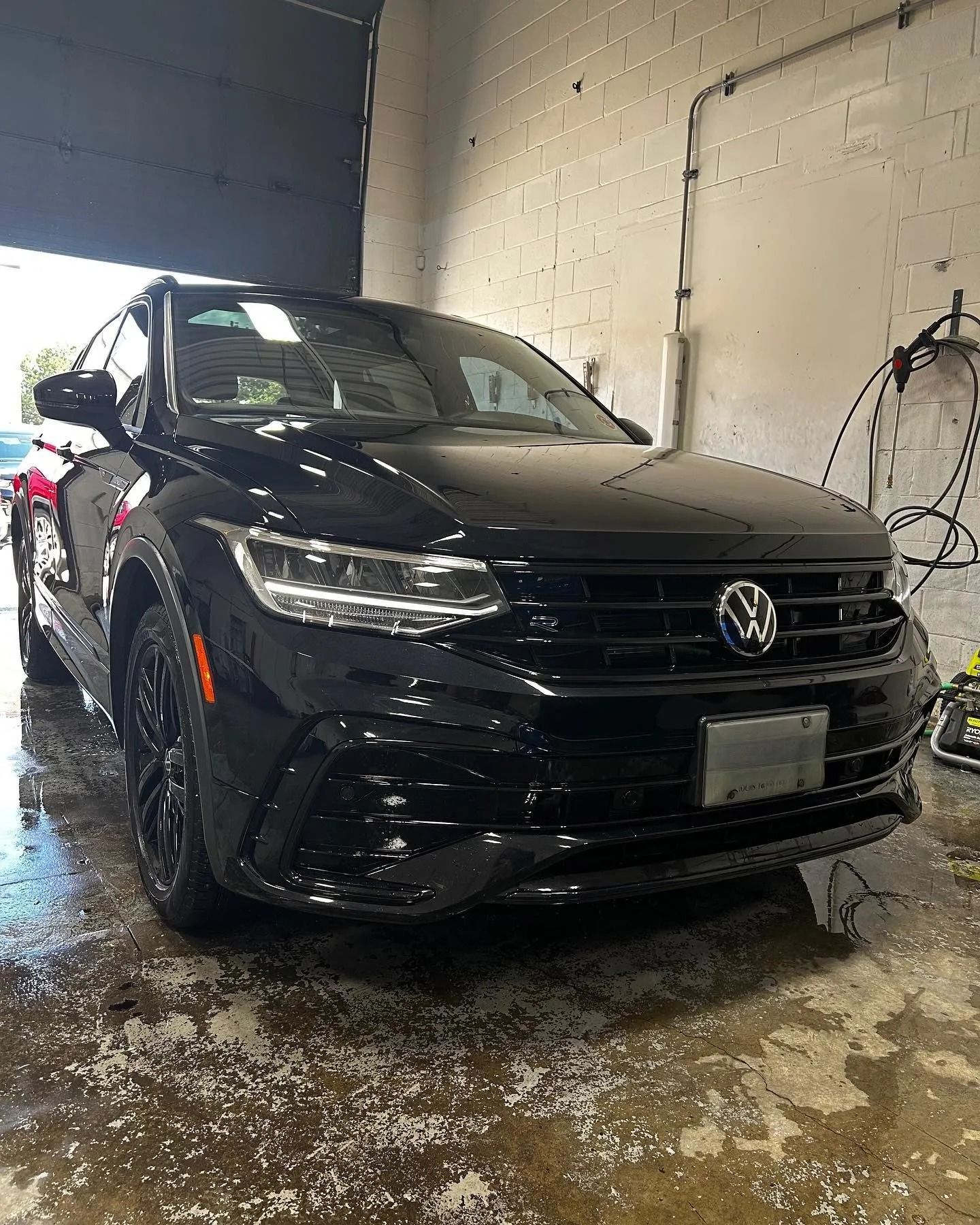 A black Volkswagen Tiguan SUV parked inside a garage with wet, reflective concrete floors.
