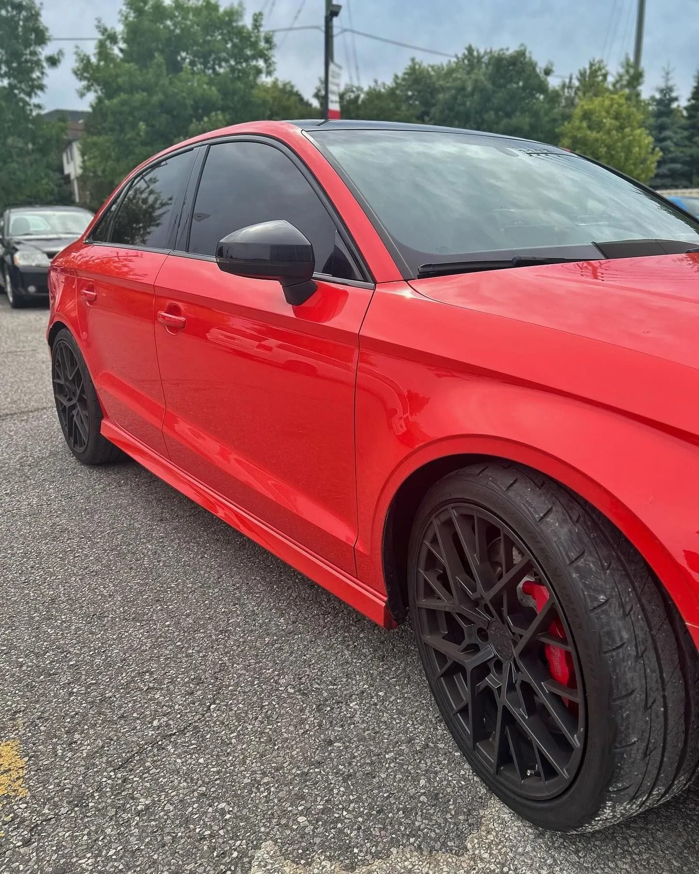 A bright red Audi sedan parked on an asphalt lot, featuring dark multi-spoke wheels and tinted windows.