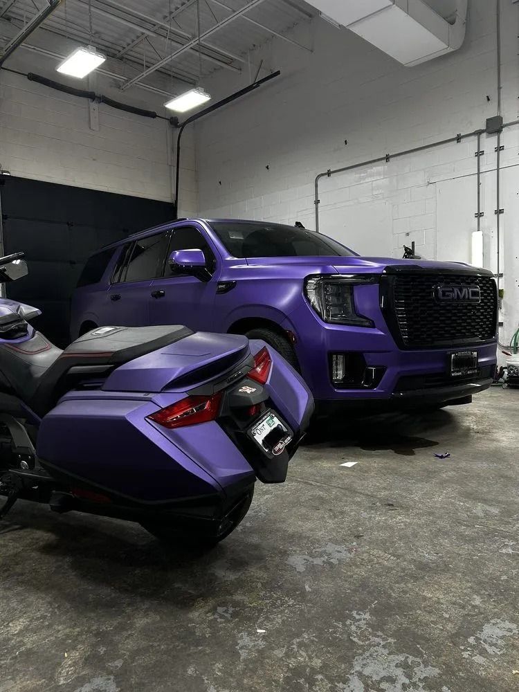 A matte purple GMC Yukon SUV parked in a garage next to a motorcycle with a matching purple finish.