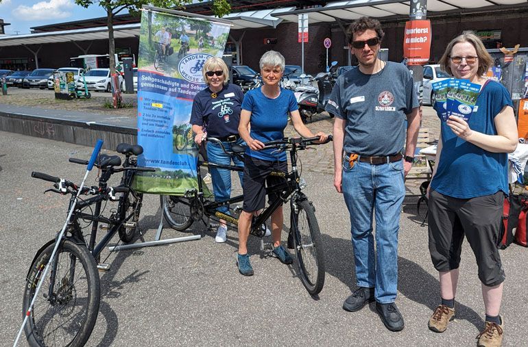 Foto von zwei Tandems und einem Banner vom Tandemclub. Daneben stehen Anja, Ulrike, Stephan und Maaike vom Tandemclub. die Flyer verteilen.