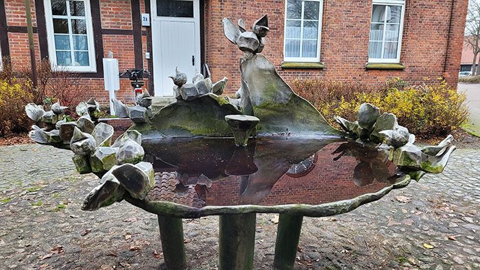 Kleine Fontaine auf Stelzen. Es formt ein kleines Wasserbecken mit darum so etwas wie Stein mit sämtlichen Spatzen darauf. Die Fontaine ist aus Metall gemacht.