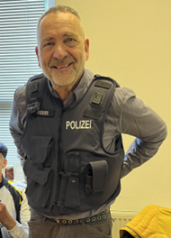 Jo mit einer Polizeiweste an. Er guckt relativ entspannt und freundlich