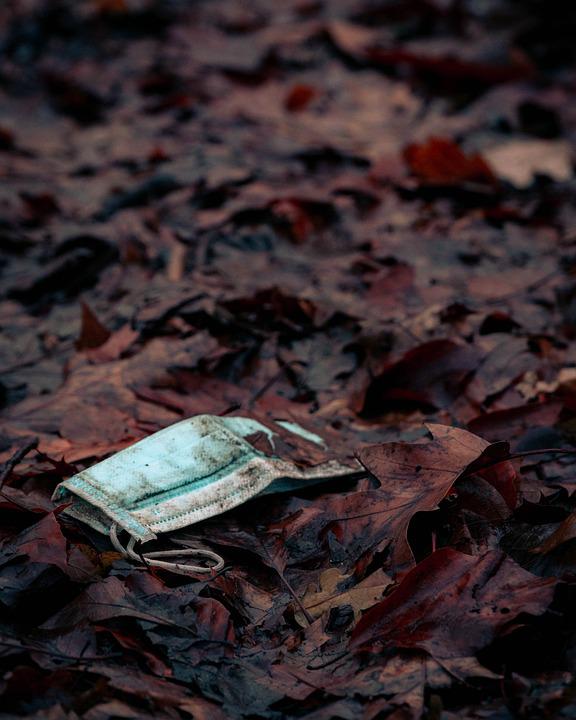 Dreckige Maske im Wald auf dem Boden, zwischen den Blättern