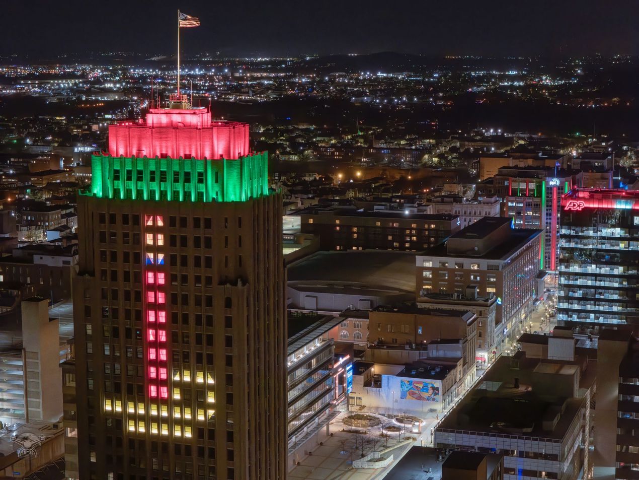 An aerial view of a city at night with a tall building lit up with red and green lights.