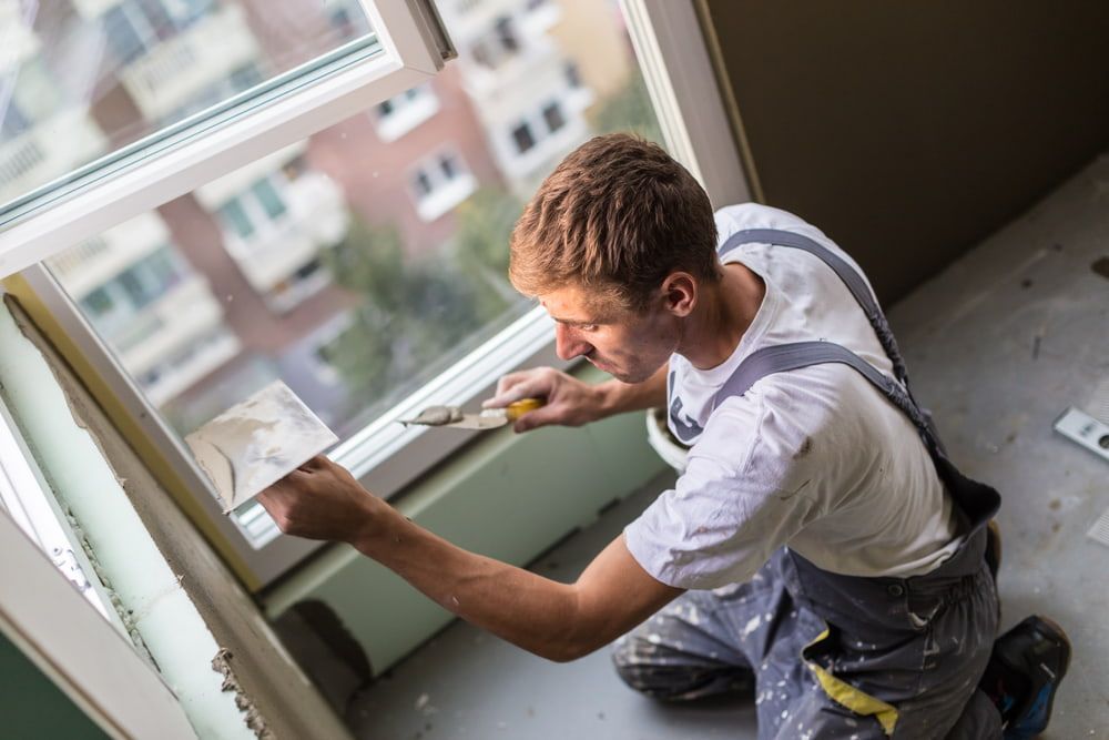 A Man is Kneeling Down and Plastering a Window Frame — Poljak Plasterers in Railway Estate, QLD
