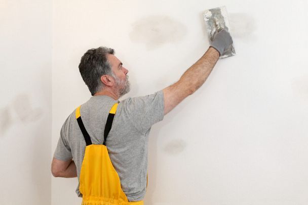 A Man is Plastering a Wall With a Trowel — Poljak Plasterers in Currajong, QLD