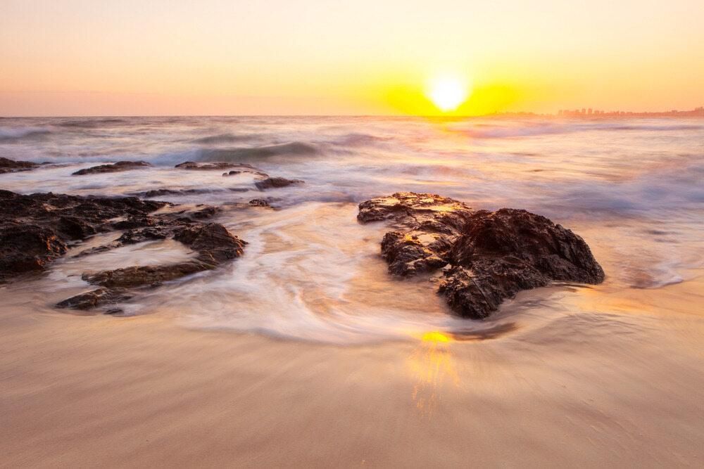 The Sun is Setting Over the Ocean on a Beach With Rocks in the Foreground — Poljak Plasterers in Kirwan, QLD