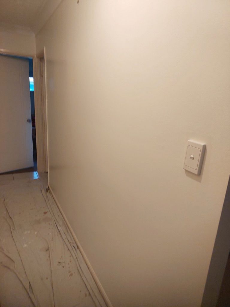 A hallway with white walls and a light switch on the wall.