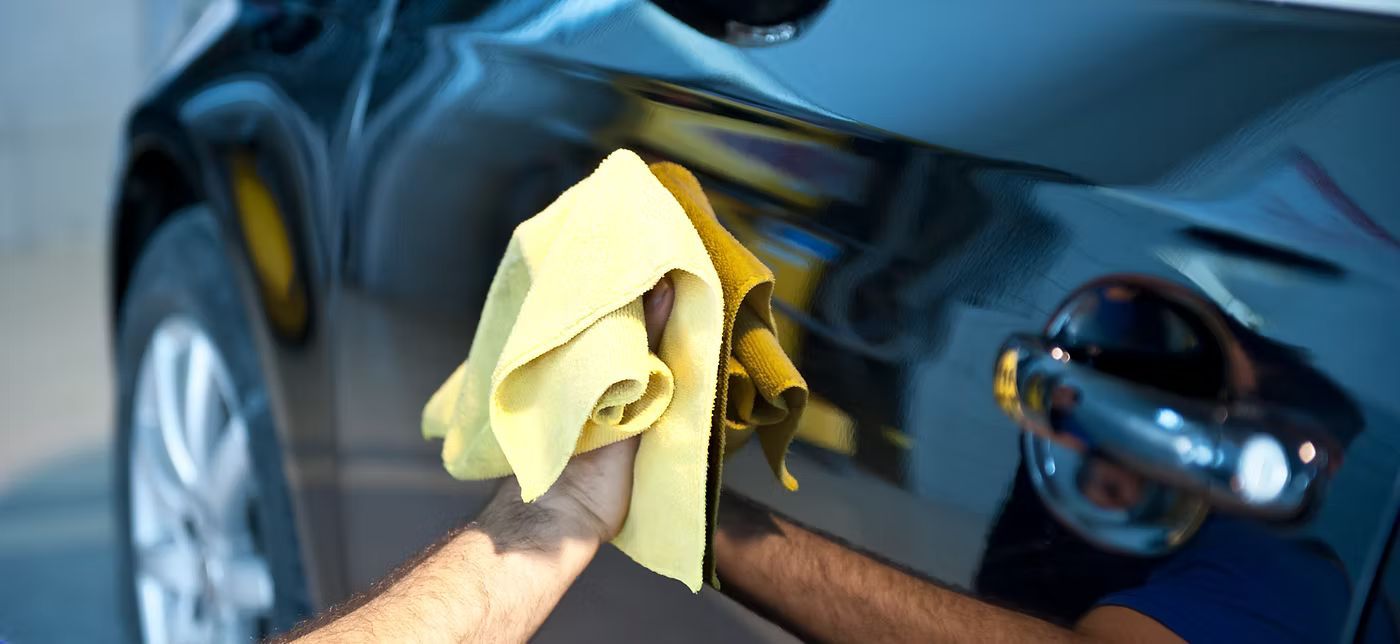 A person cleaning a black car with a yellow cloth.